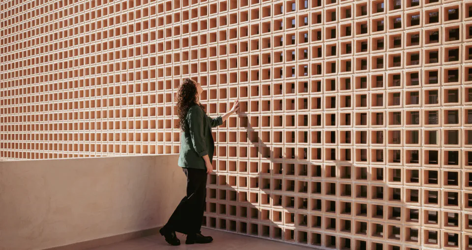A woman resting her hand on the terracotta ceramic lattice façade